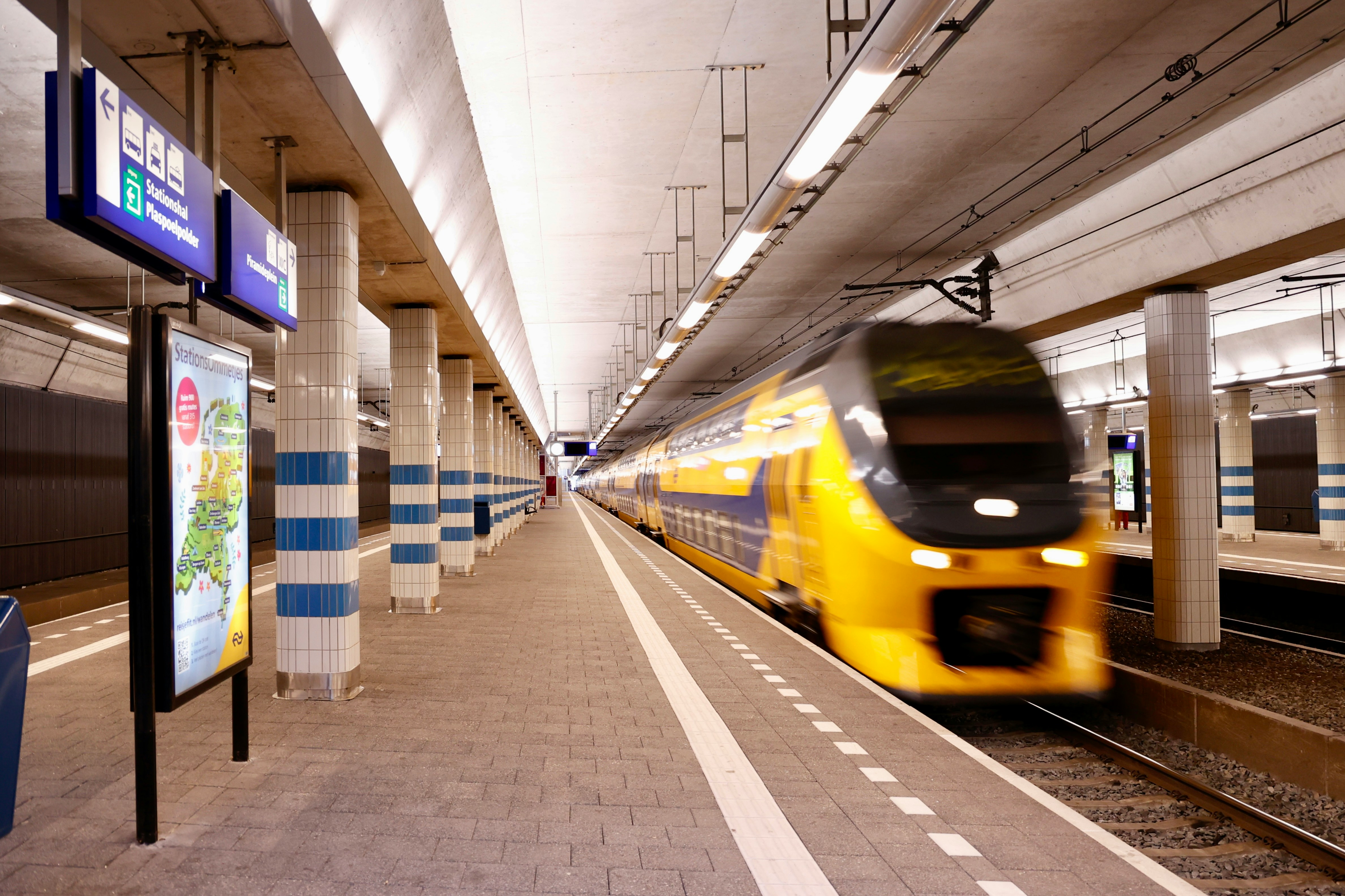 A yellow and blue train arriving beside a station platform